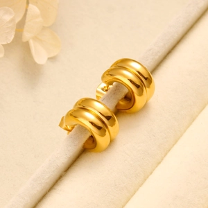 Close-up of golden double-layered C-shaped hoop earrings on a beige display stand