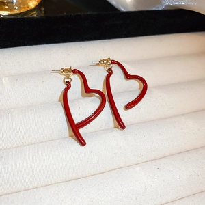 Detail view of heart-shaped hollow earrings with deep red finish and gold studs on a tray