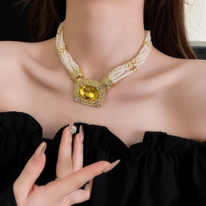 Dettaglio di collana di perle multistrato con grande ciondolo in gemma giallo oro