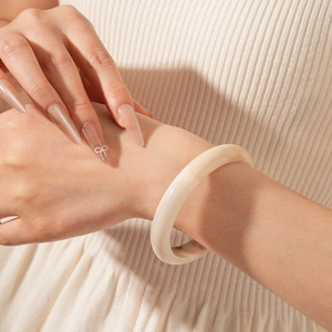 Close-up of a minimalist cream resin bangle worn on the wrist against white knit fabric