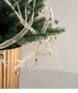 Dettaglio di nastro in organza crema con perline d'oro su rami verdi di albero di Natale