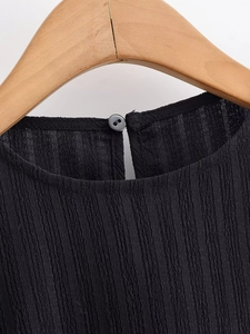 Détail du tissu plissé noir montrant le bouton du col et la découpe en goutte