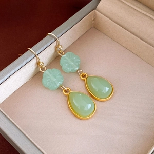 Detail of green leaf zircon earrings with gold plating and teardrop pendant on beige velvet