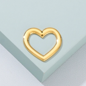 Macro shot of a hollow gold heart pendant with dual holes on a geometric stand