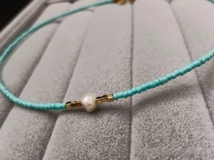 Detail of turquoise beaded necklace with freshwater pearl and golden square spacers