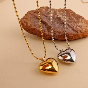 Polished gold and silver heart necklaces with bead chains on natural rock background