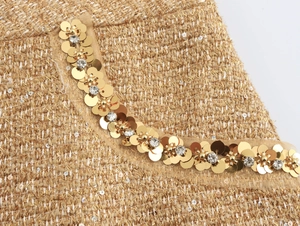 Detail of tweed collar with gold sequins and rhinestones on a white background