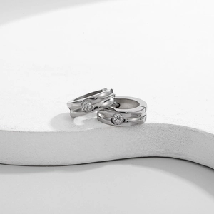 Macro detail of silver hip-hop earrings with clear zircons on a white stone pedestal