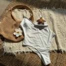 Flat lay of white one-piece swimsuit with beach accessories on a textured woven background
