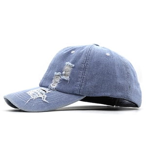 Détail d'une casquette en denim bleu clair avec anneaux métalliques et déchirures usées