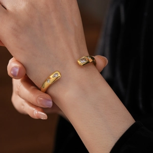 Detail of a gold-plated open bangle featuring clear zircon stones worn on a model wrist