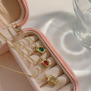 Three gold vintage necklaces with green, red and white square pendants in a pink jewelry box