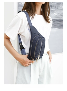 Detail of dark blue quilted crossbody bag with gold zippers and adjustable strap