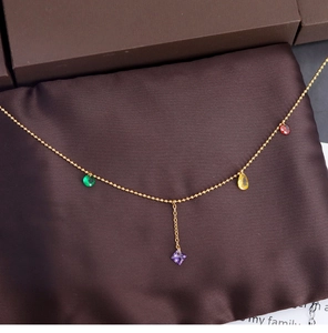 Close-up of golden beaded necklace with colorful gem pendants on brown silk cushion