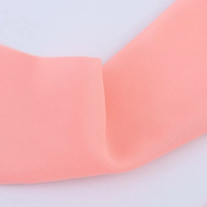 Close-up of coral pink chiffon fabric texture with delicate pleats and soft drape