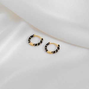 Detailed close-up of golden geometric hoop earrings with black enamel drip on white satin