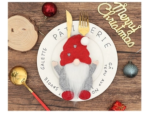 Detail of a gnome-style Christmas cutlery holder with red knit hat on a white dinner plate