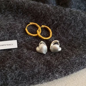 Golden wavy hoop earrings and silver matte heart earrings on dark knit background