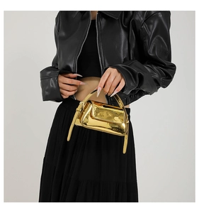 Detail of a mini gold baguette bag with a metallic mirror finish and top handle strap