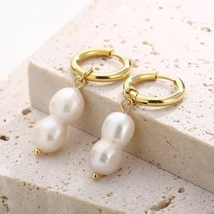 Gros plan de boucles d'oreilles perles avec anneaux dorés sur fond de pierre neutre