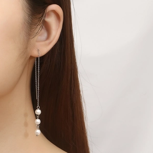 Detail of silver tassel chain earrings with three white pearls worn by a model