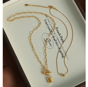 Detail of layered gold necklace featuring OT buckle lock pendant and snake chain in box