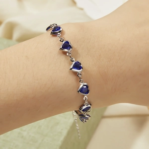 Detail showing deep blue heart gemstones on a polished silver chain bracelet with clasp