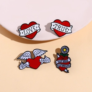 Close-up of heart-shaped enamel brooches with wings and ribbons on a beige stand