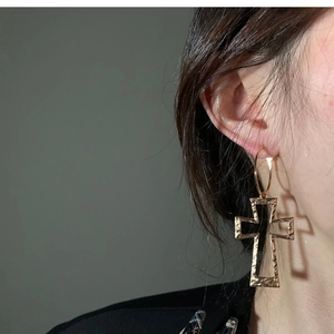 Close-up of golden cross pendant hoop earring with hammered metal texture on model