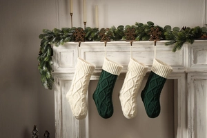Detail of knitted Christmas stockings in white and dark green hanging on a white fireplace