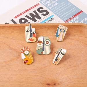 Macro view of five Picasso-style enamel face brooches on a light wood tray with newspaper