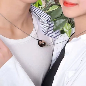 Close-up of interlocking black and gold cat heart pendants for couples on silver chains