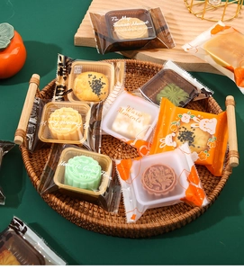 Assorted mooncakes in colorful plastic gift packaging on a rustic woven tray