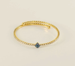Detail view of a 18k gold-plated open bangle with blue square gemstone and zircon accents