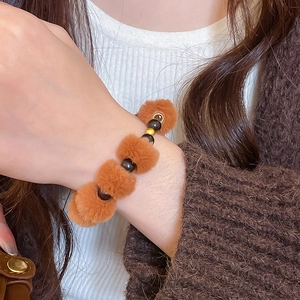 Détail du bracelet d'hiver avec perles polies et pompons en peluche marron sur le poignet
