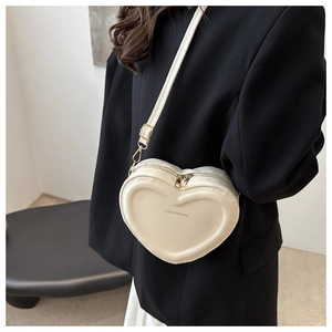 Side view of a white heart-shaped crossbody bag with adjustable strap on a female model