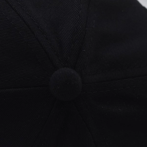 Détail macro du bouton supérieur de la casquette noire et texture du sergé de coton
