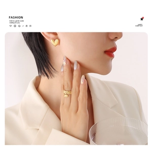 Detail of gold heart earrings and leaf ring worn with a white professional blazer