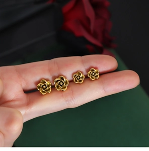 Macro view of gold rose earrings in two sizes shown against a deep green backdrop