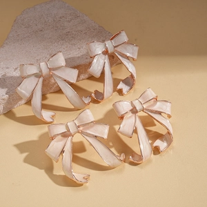 Vintage cream bow earrings with rose gold trim on decorative warm stone display