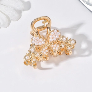 Close-up of a golden butterfly hair claw clip with white pearls on a white background