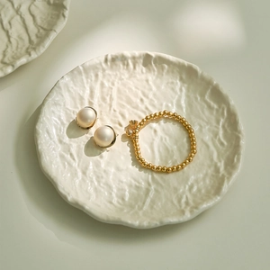 Elegant gold bead bracelet and pearl earrings set displayed on a white textured ripple tray