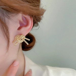 Close-up of model wearing gold rope knot earrings with a metallic woven texture