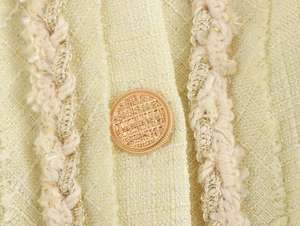 Détail de boutons en métal doré et bordure tissée sur le tissu en tweed jaune de la robe