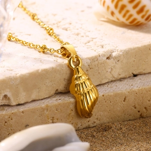 Macro view of gold shell pendant on stainless steel chain over beach sand and stone