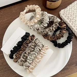 Detail of satin hair scrunchies set in neutral colors displayed on a ceramic tray
