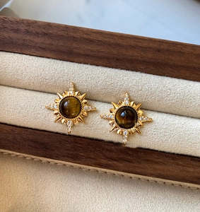 Détail macro de boucles d'oreilles étoile en or 18K avec oeil de tigre et micro-zircons