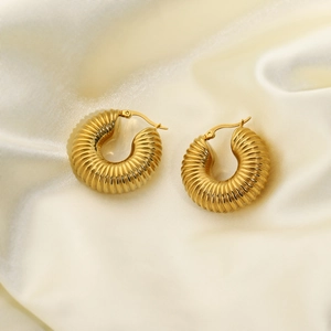 Textured gold-plated stainless steel hoop earrings on elegant silk fabric background