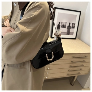Side view of a black patent leather shoulder bag with a gold horseshoe buckle on a model