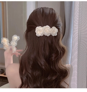 Detail showing three white satin camellia rose hair clips on long wavy hair